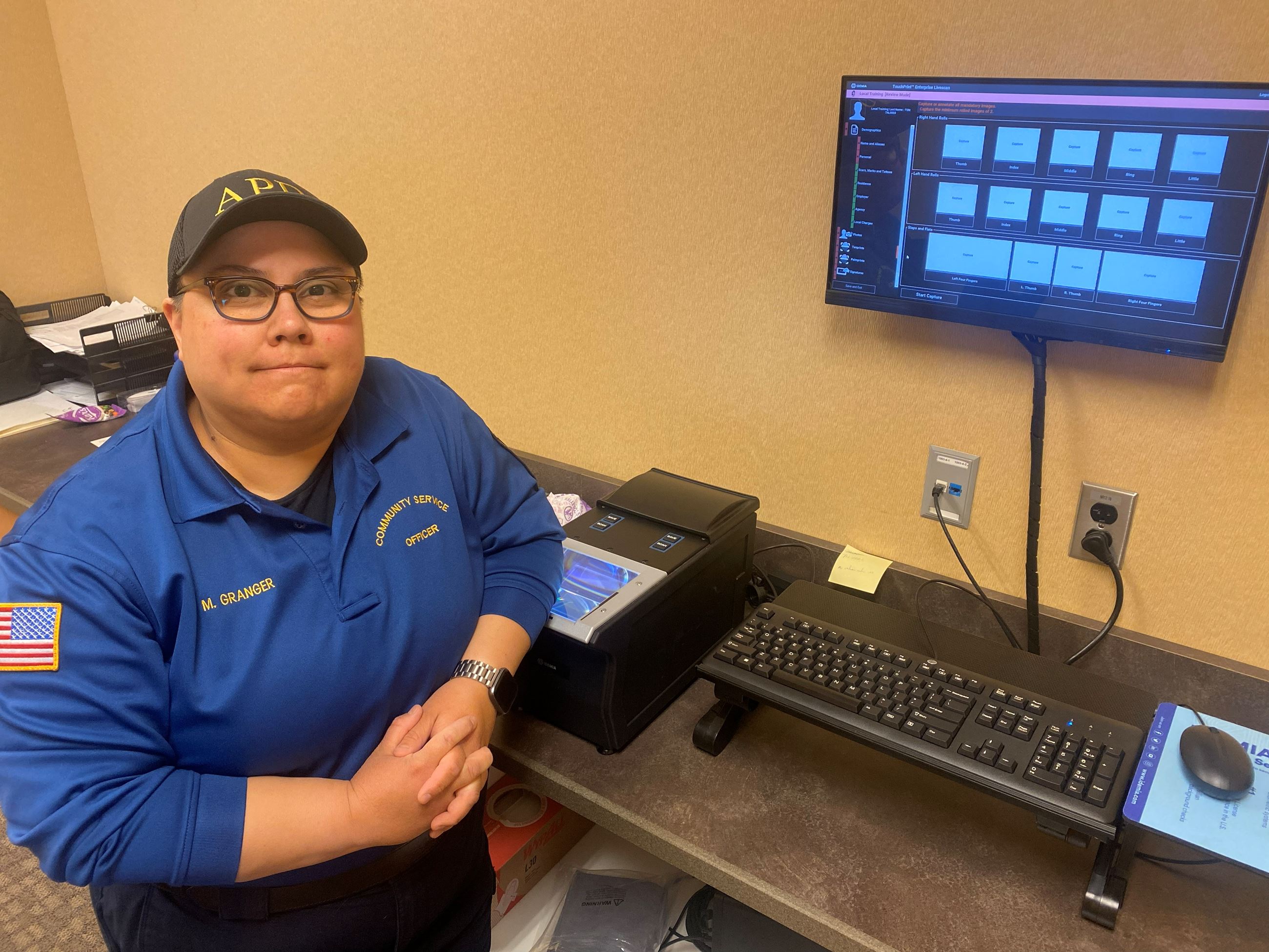 Community Service Officer posing next to a fingerprint scanner in an office.